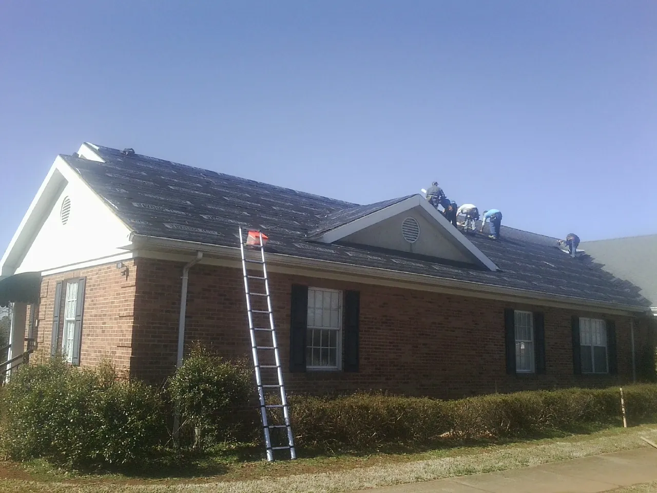 Crew tearing shingles off a brick ranch roof with a ladder set — Metal Roof Repair work by our crew in Hurleyville