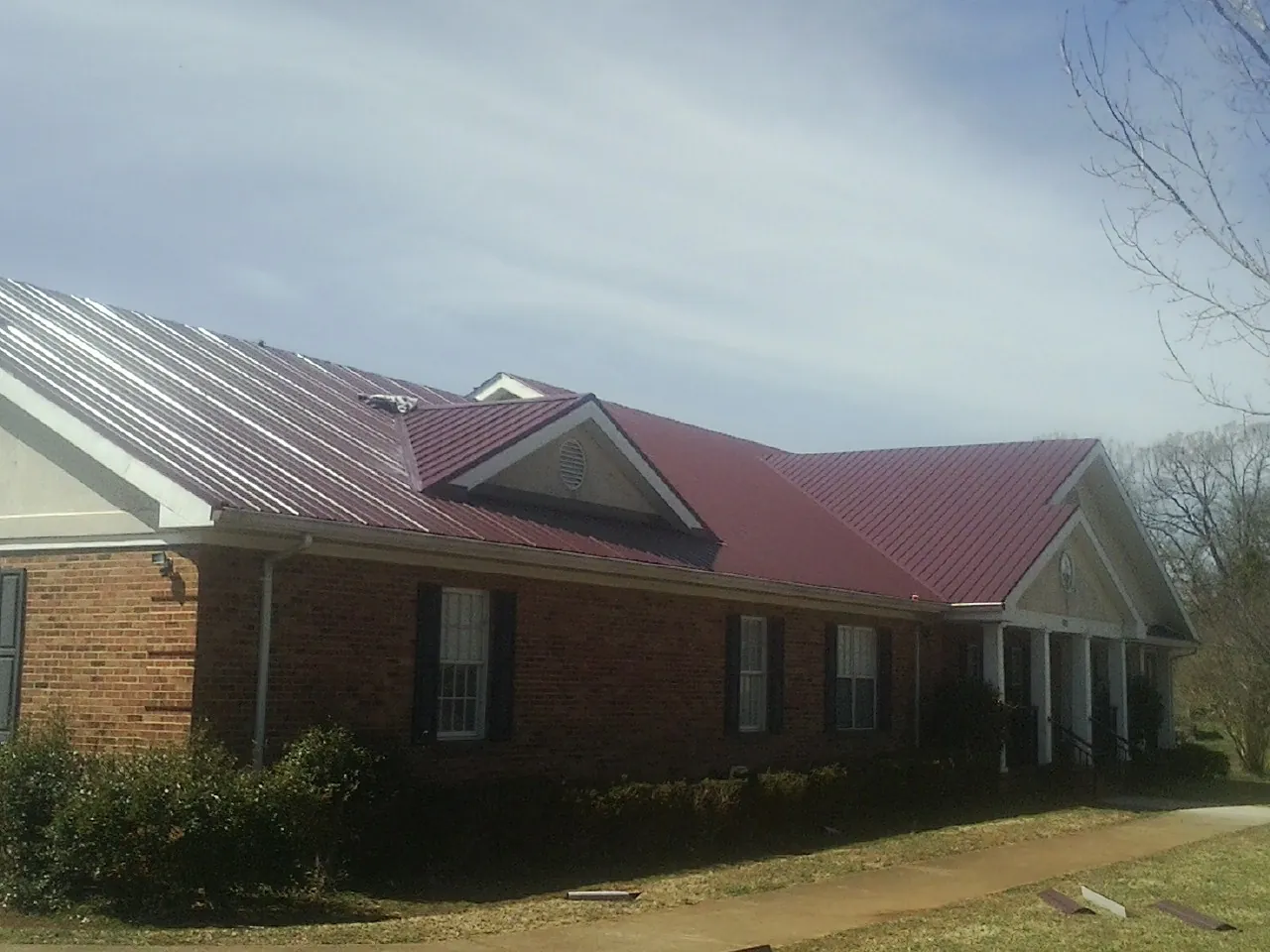 Red metal roof with gabled entries on a long brick building, from a Hail Damage Roof Repair job in Hurleyville