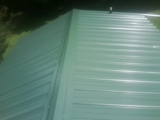 New green metal panels meeting at the ridge of a roof — Flat Roof Repair work by our crew in Hurleyville