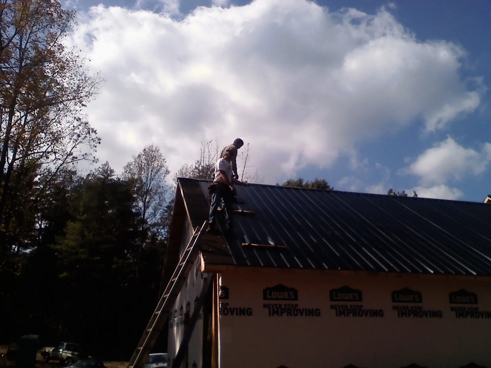 Roofer fastening dark metal panels high against a cloudy sky, from a Roof Inspection job in Hurleyville