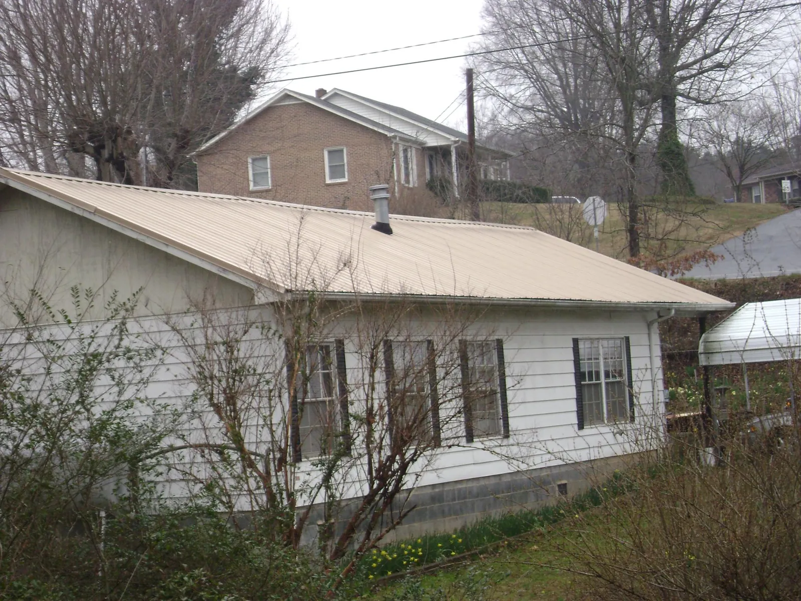 Tan metal roof on a white sided house set into a hillside — Commercial Roofing by Roofing Brothers in Hurleyville